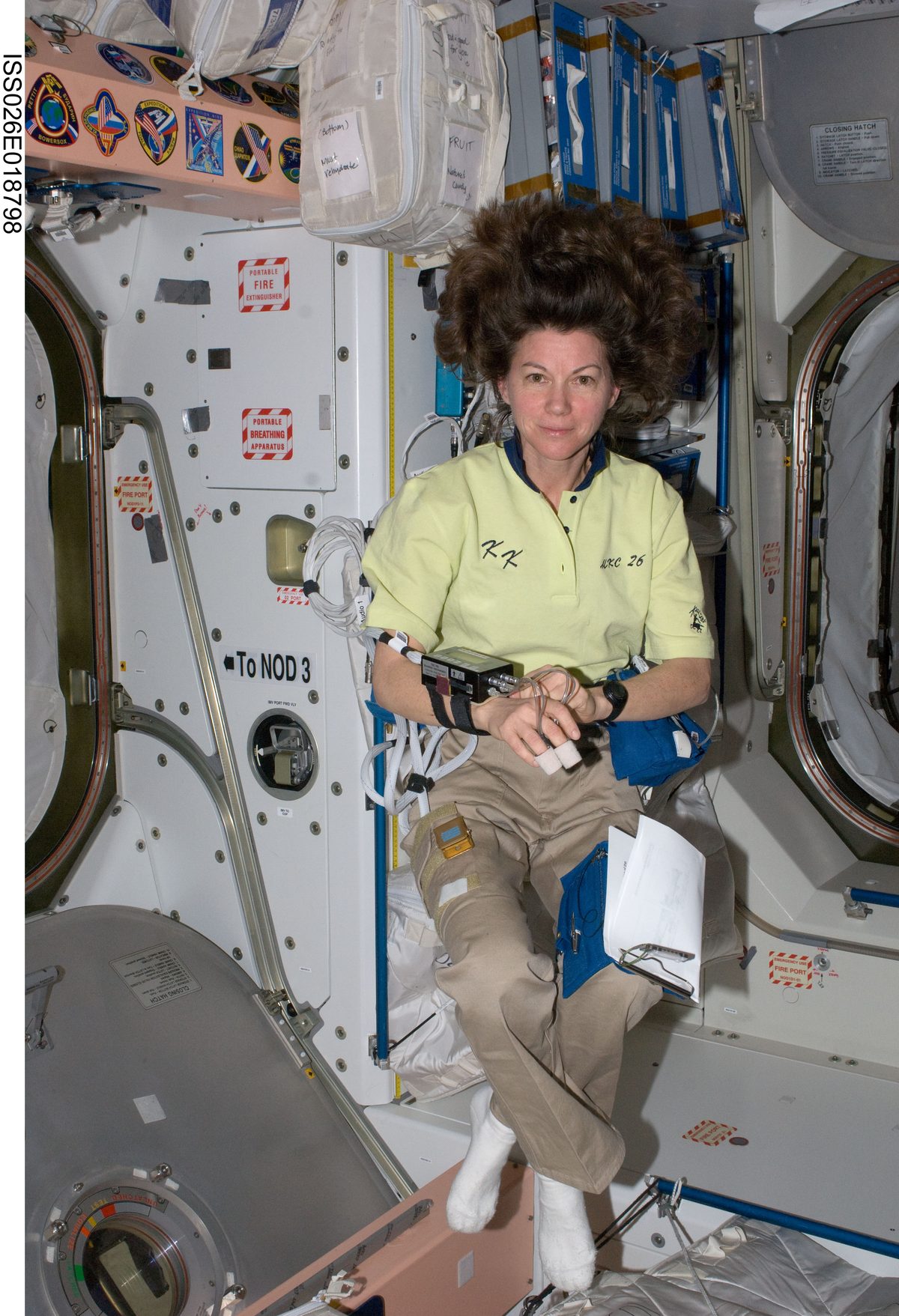 Astronaut Cady Coleman floating in a space station module, wearing chest electrodes, a recorder and a blood-pressure cuff.
